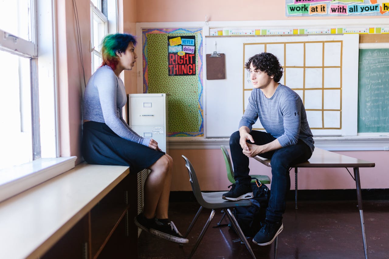 Two students engaged in a conversation in a classroom setting, reflecting an educational environment.